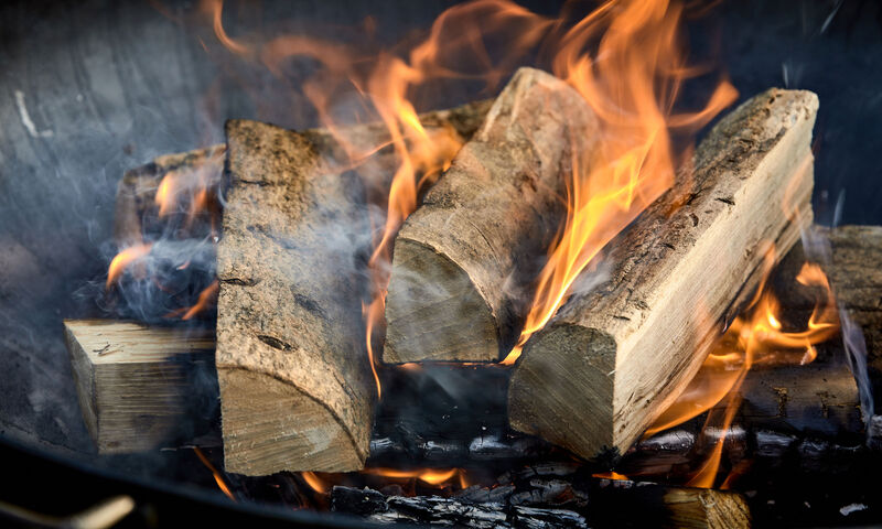 Recently lit fire with logs of flaming wood on a bed of chopped kindling in a portable summer barbecue in a close up panorama banner view